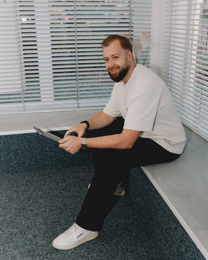 Tobias Mantsch sitzt entspannt mit Tablet am Fenster der Agentur